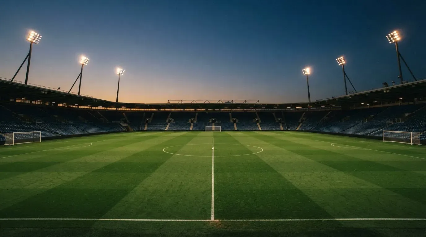 An empty football stadium with floodlight masts at dusk
