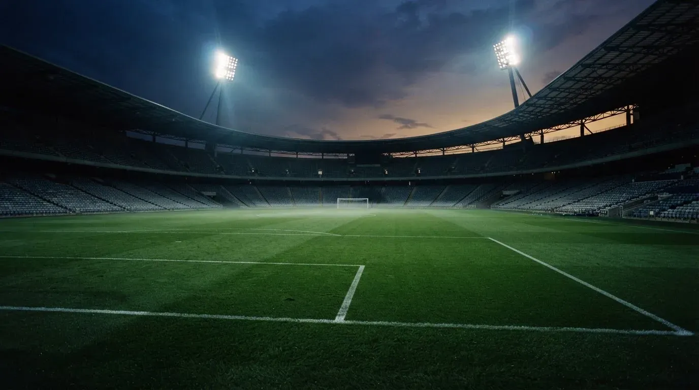An empty football stadium with floodlight masts at dusk
