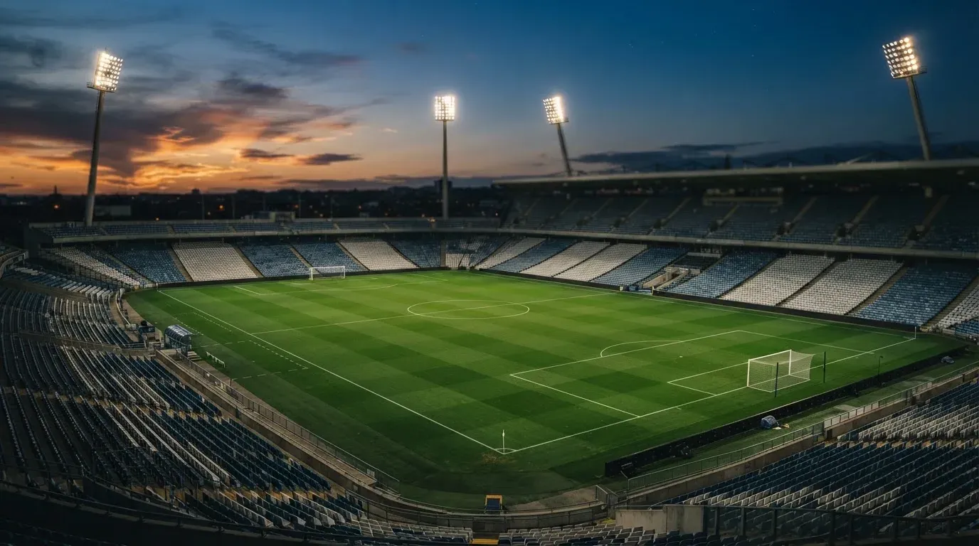 An empty football stadium with floodlight masts at dusk