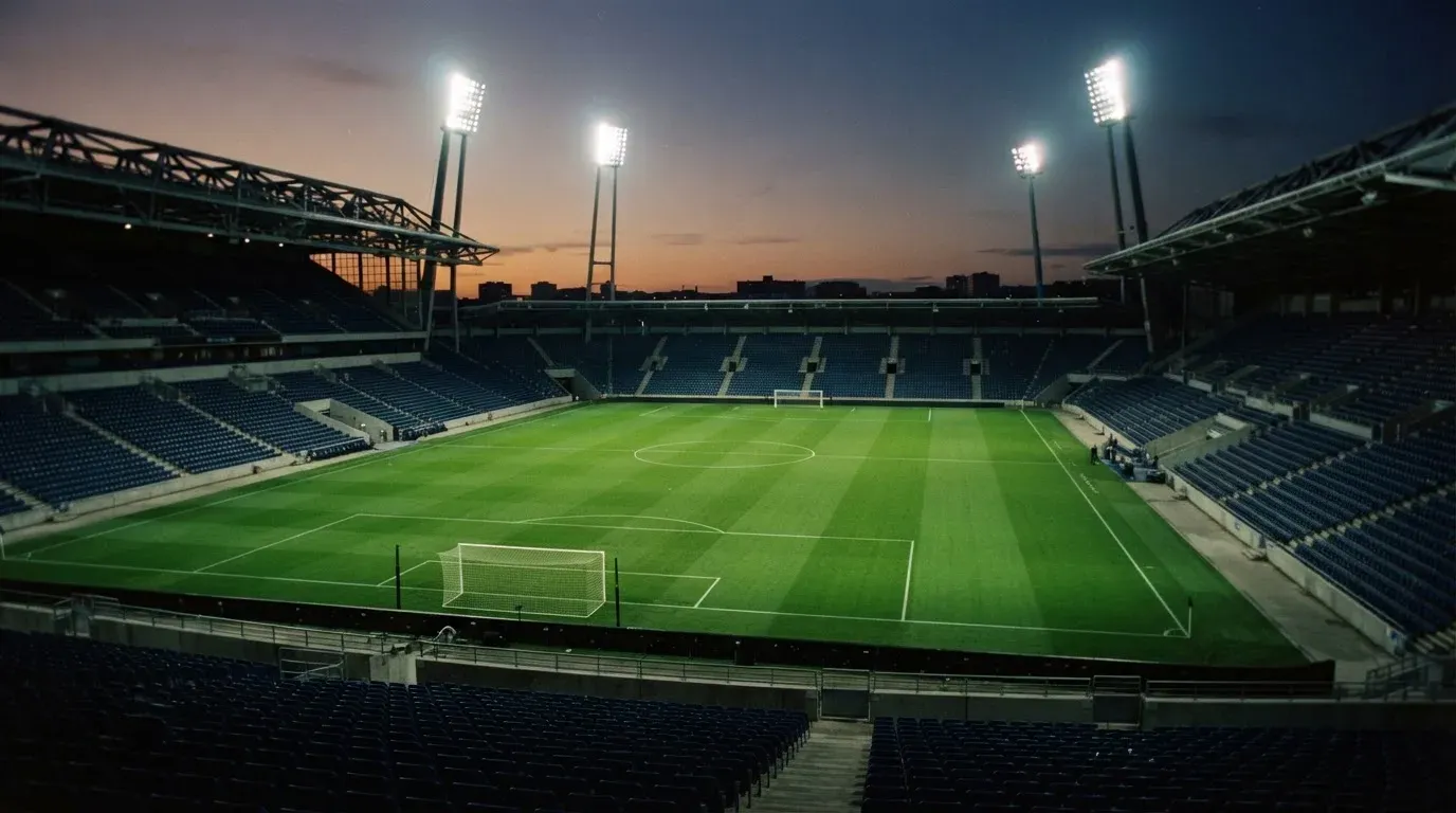 An empty football stadium with floodlight masts at dusk