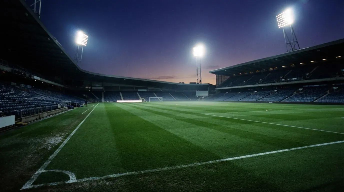 An empty football stadium with floodlight masts at dusk