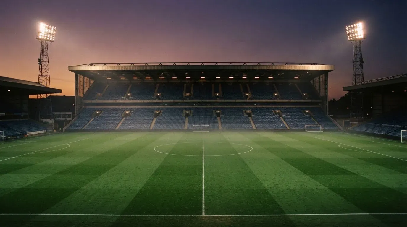 An empty football stadium with floodlight masts at dusk